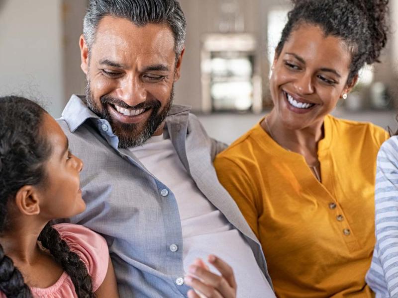 Cheerful couple at home in the living room are sitting on sofa relaxing and laughing together with their two daughters. 