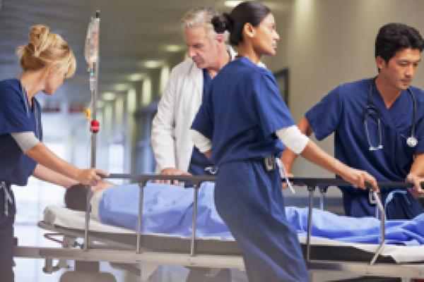 Doctor and nurses wheeling patient in gurney through hospital corridor  - stock photo