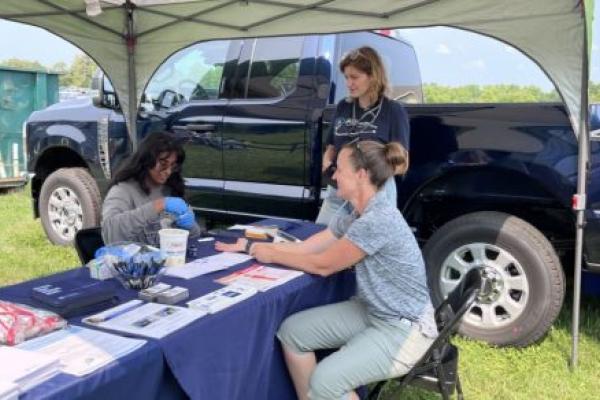 Students and faculty sit at a tent at at an exhibition, providing health care screenings and edcuation