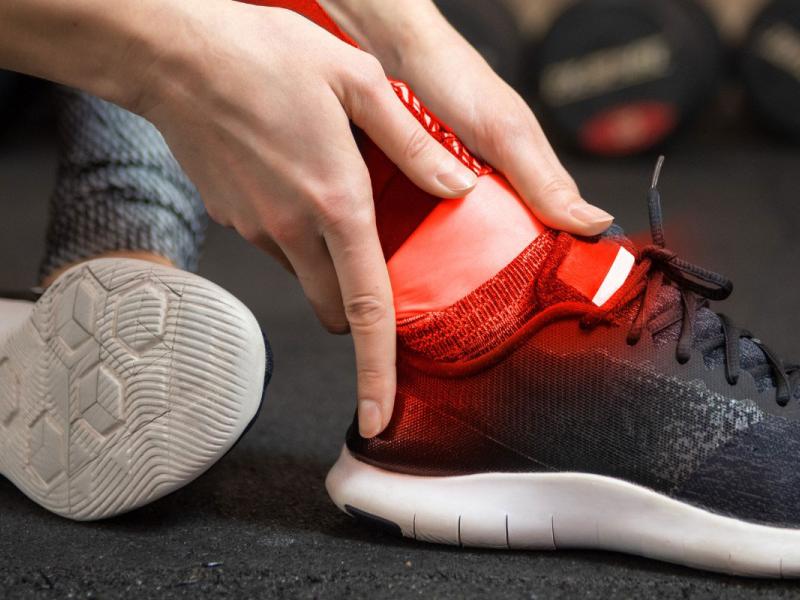 A person sitting on the floor holding their ankle with red light area shown around the ankle to show possible pain.