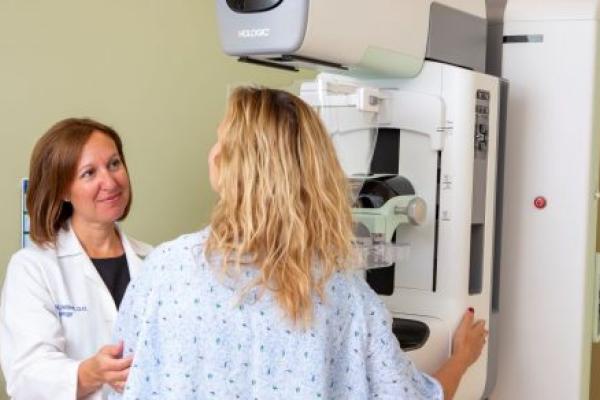 Dr. Alison Chetlen, left, touches a patient’s arm as she positions her in front of a mammography machine. Chetlen is wearing a white coat with her name and “Radiology” on the upper-right.