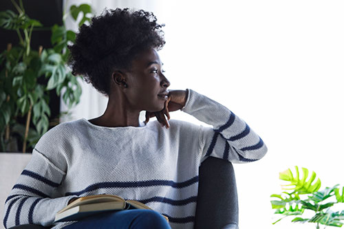 Young woman sitting in armchair, hand on chin, contemplating about a book she is reading