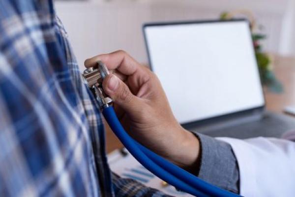 A doctor listens to a male patient’s heart during a medical examination. Close-up view of the doctor’s hand holding the stethoscope.