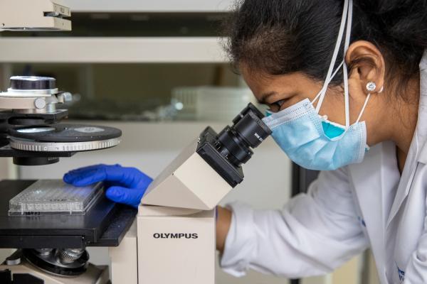 A member of the Penn State Health lab team reviews samples on a microscope.