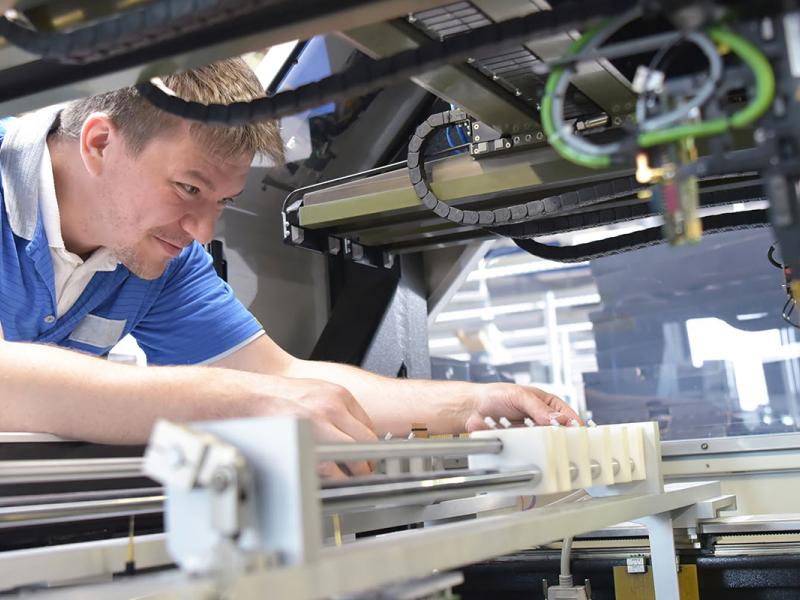 Engineer enjoying his Penn State Health job working on a machine for semiconductor boards.