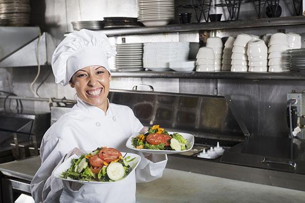 Female Hispanic chef (30s) in commercial kitchen, preparing gourmet salad.
