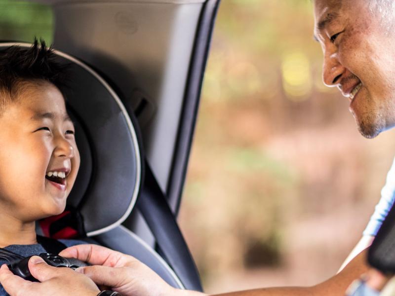 Father buckling son in car seat.