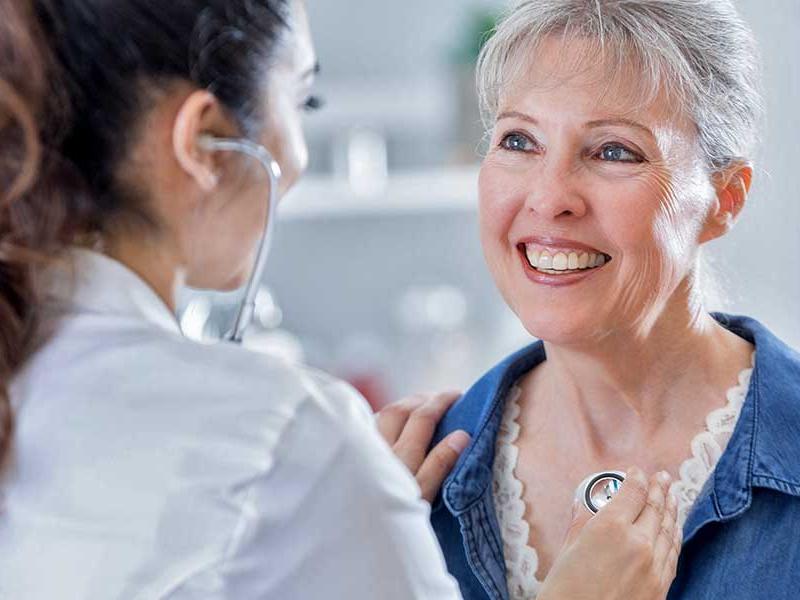 Female doctor listens to female patient's heart during a medical exam.