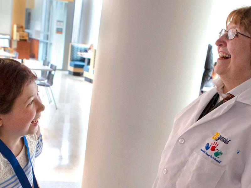 Female physician with white lab coat with blue colored hand print while child is laughing.