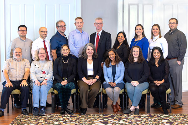 A group of people some sitting on chairs and some standing posing for the camera.