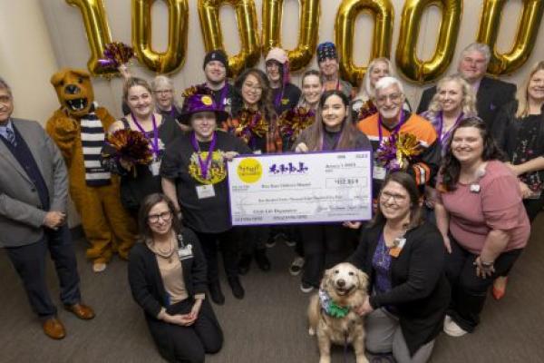 Eighteen people – along with a dog and a costumed Nittany Lion – pose with a check made out to Penn State Health Children’s Hospital in the amount of $112,854, from Spirit of Children. Large gold inflatable numbers spelling out “1,000,000” are on the wall directly behind them.
