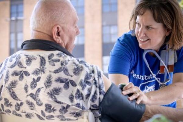 A community health nurse at 澳洲彩票官网 smiles at a man as she checks his blood pressure. She is wearing a T-shirt and has a stethoscope around her neck. He is wearing a shirt with a leaf print on it.