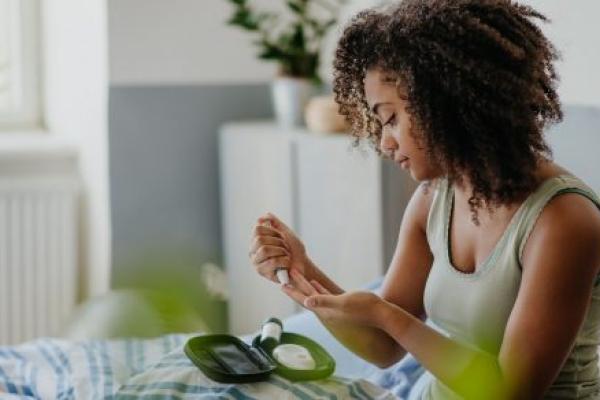 A young woman tests her blood sample on a blood sugar meter at home.