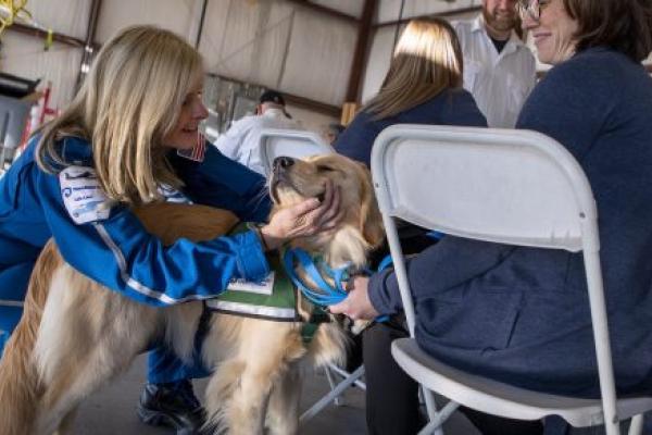 A woman pets a dog next to a woman seated in a chair.