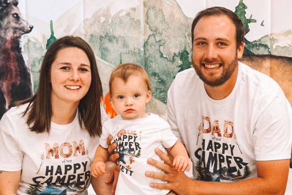 A woman and man sit with a toddler boy between them, held by the man. 