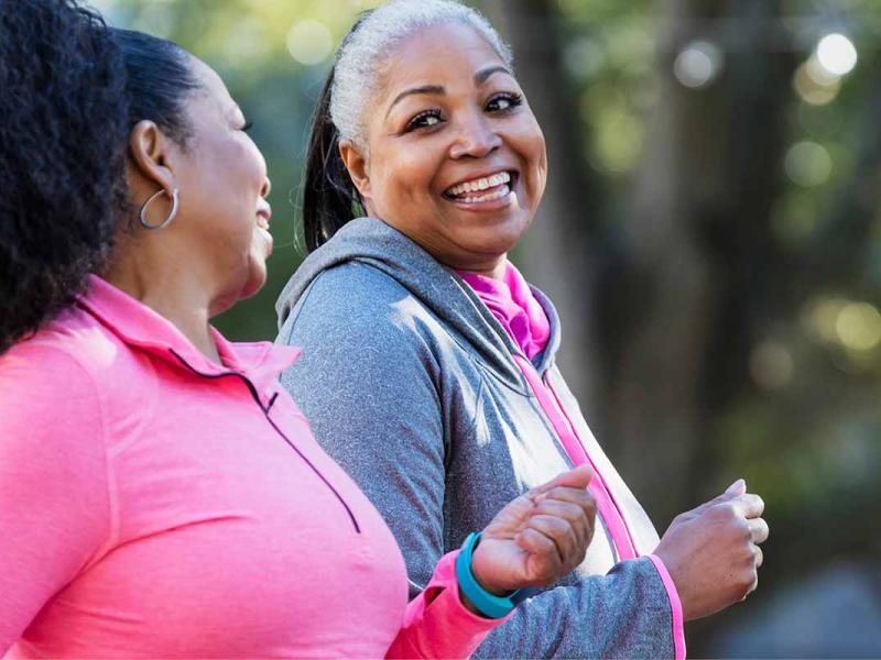 Two women are walking outdoors. They are talking and smiling as they walk.