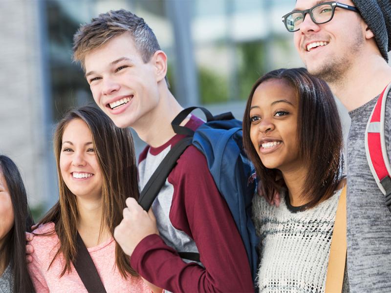 A group of teen boys and girls with backpacks stand together and smile.