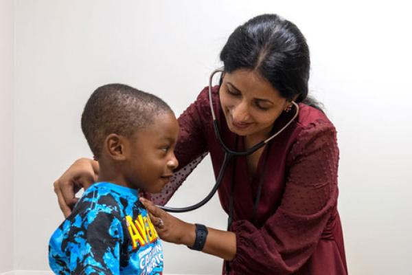 Female provider examining young child as mother is sitting in a chair in an exam room.