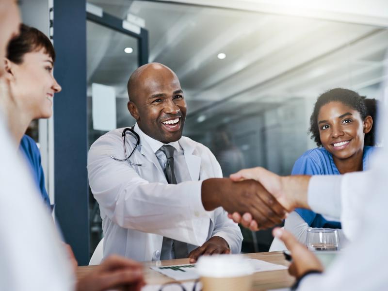 A physician shakes the hand of another as they talk to a recruiter.