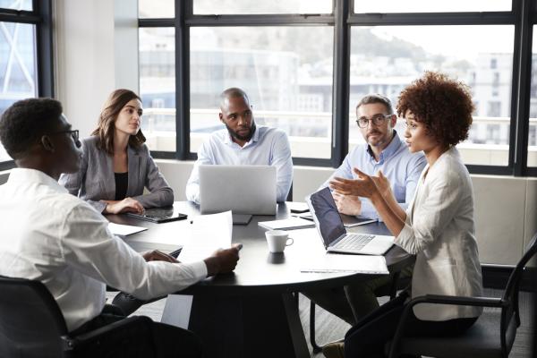 Employees gather around a table in a conference room for a meeting.