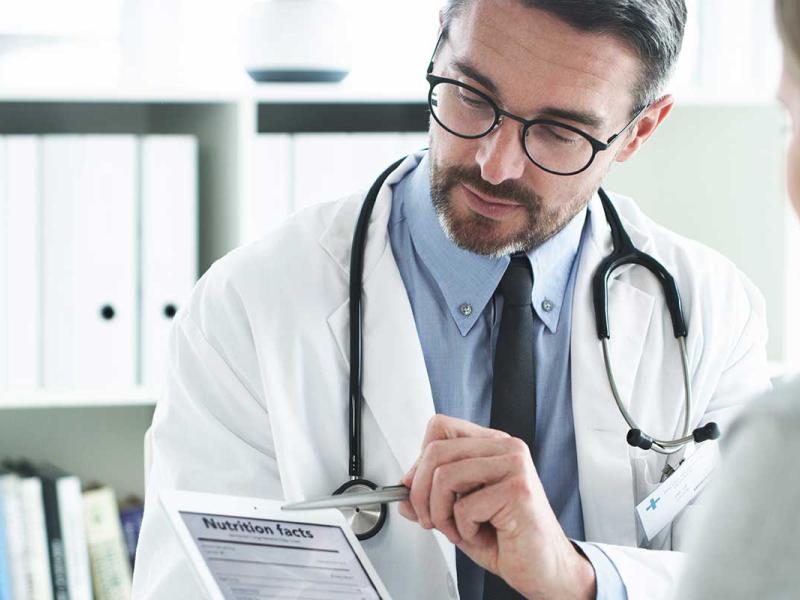 Male doctor explaining a nutritional facts table on a digital tablet to a female patient in his office.
