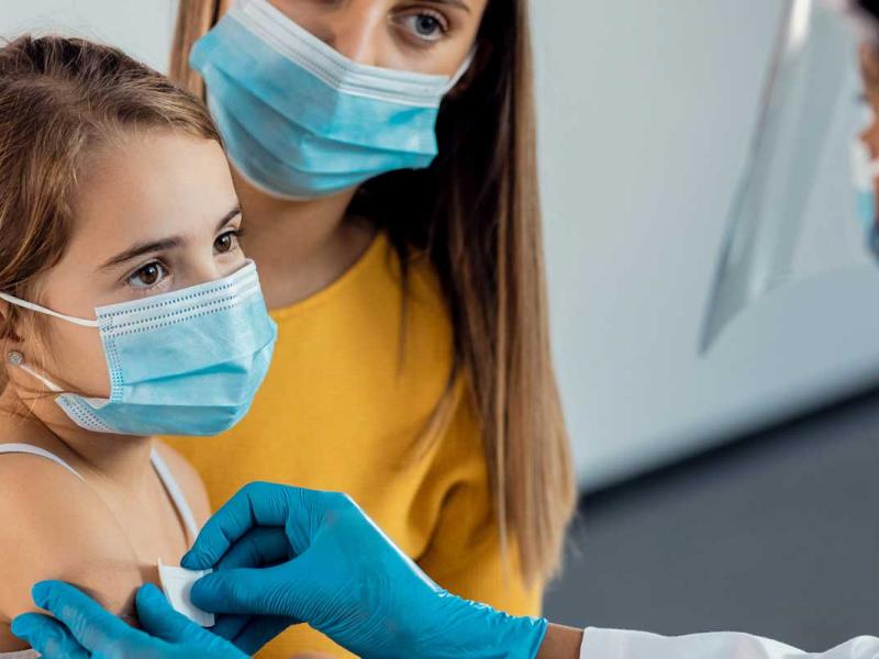Female doctor placing adhesive bandage on little girl's arm after vaccination. Focus is on girl.