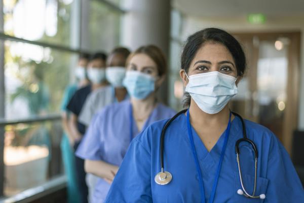 Nurses in masks stand in a row, looking at the camera.