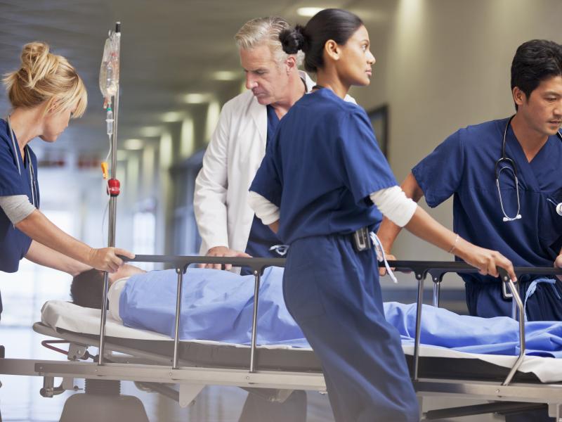 Advanced practice healthcare professionals roll a hospital bed down a hallway.
