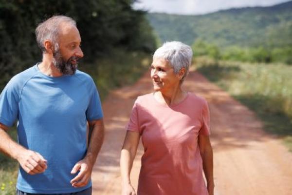Mature couple walks together in nature on sunny day.