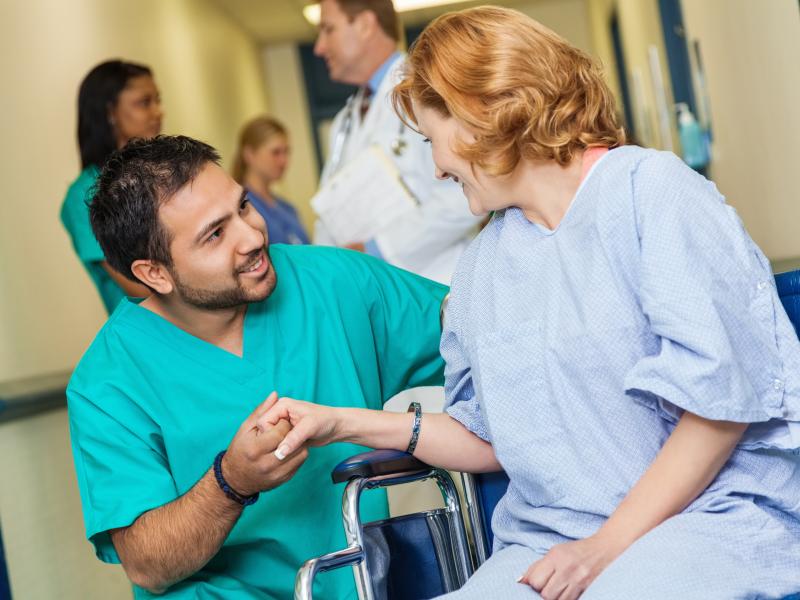 An allied health professional speaks to a patient in a wheel chair.