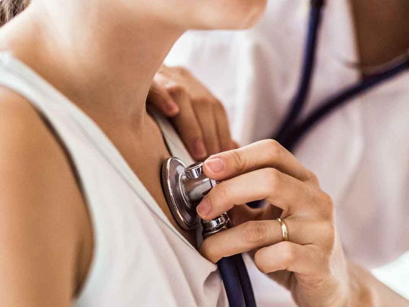Closely cropped view of unrecognizable young female doctor examining a patient’s heart with a stethoscope in her office. 