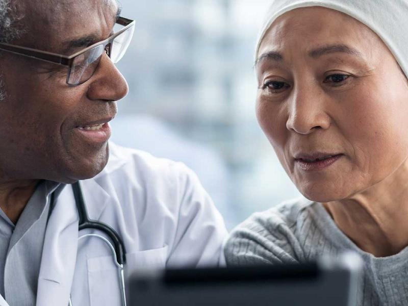 A female cancer patient and male doctor review test results on an electronic wireless tablet.