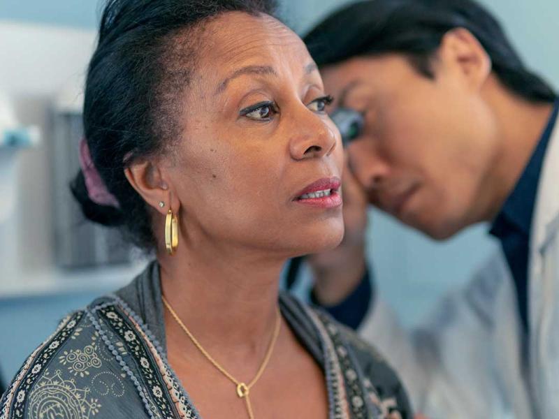 A female patient is sitting on a medical examination table in a clinic. A male doctor is checking her ears. 