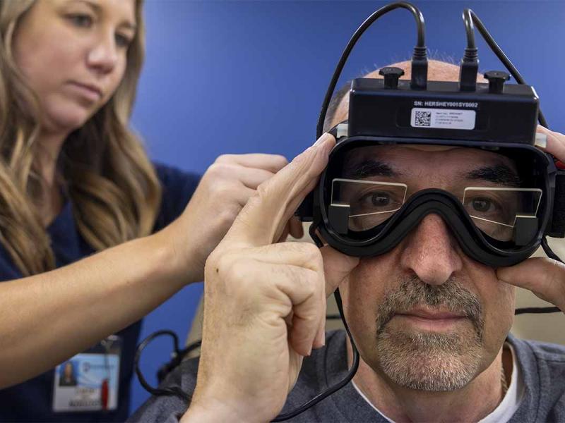 An audiologist places goggles on a patient in preparation for videonystagmograpy (VNG) testing.