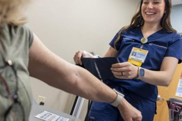 a certified medical assistant at Penn State Medical Group – assists a patient by taking their blood pressure. She is wearing blue scrubs and a name badge.
