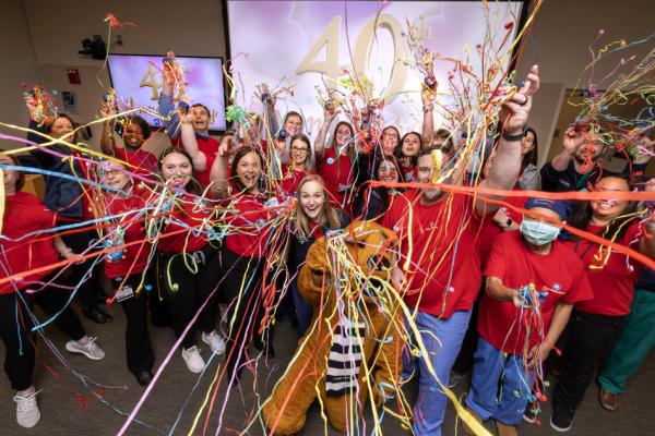 A large group of people wearing red shirts celebrating with colorful streamers in a festive event, marking a 40th anniversary displayed on a screen in the background
