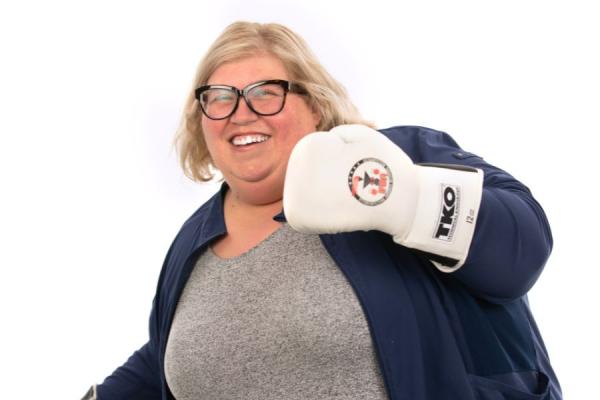 Young female posing with a boxing glove on her left hand with a smile on her face.