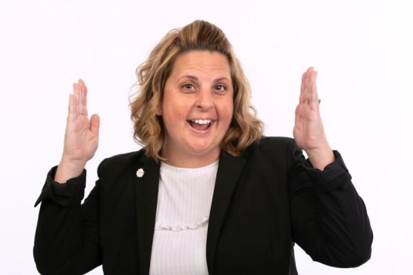 Young female posing in a dark blazer holding her arms in the shape of a football goal post with a smile on her face.