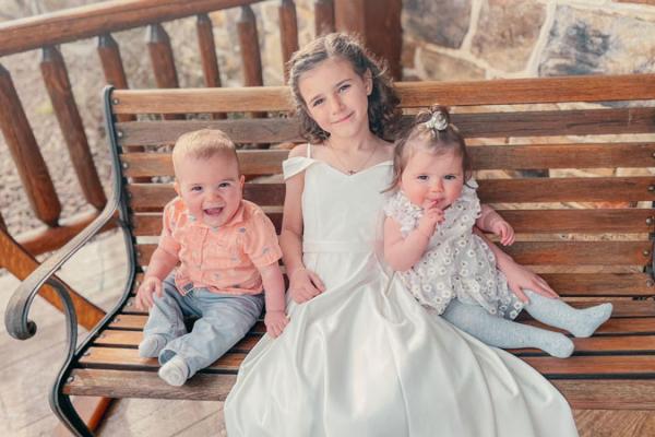 Two infants and a young child sitting on a bench outside.