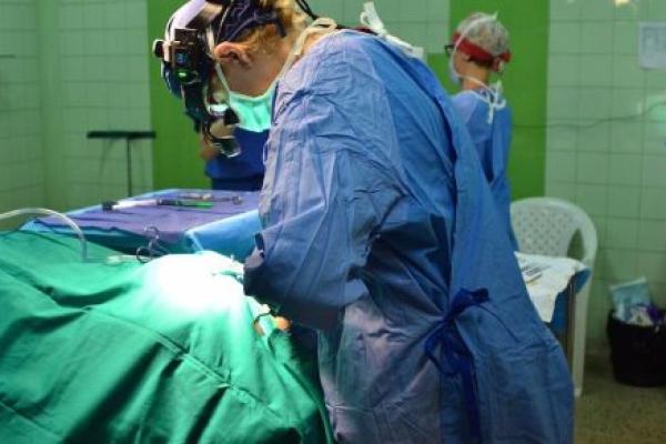A surgeon works on a patient in an operating room with tile walls.