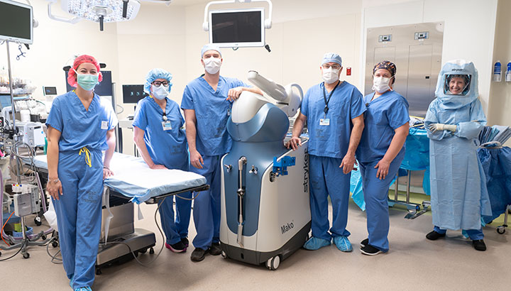 An orthopedic surgeon stands with his team and the Mako robot-assisted system for joint replacement in the St. Joseph Medical Center operating room.