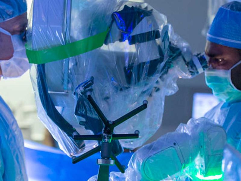 Two people in surgical scrubs look into a robot while performing a surgery