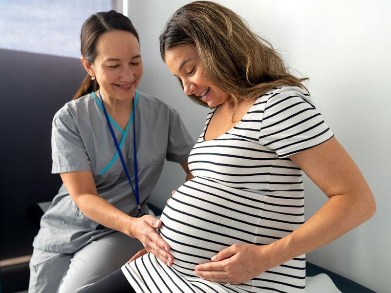 Close up shot of an expectant mother with her hand on her abdominal. Obstetrician is gently pressing on patients abdominal.
