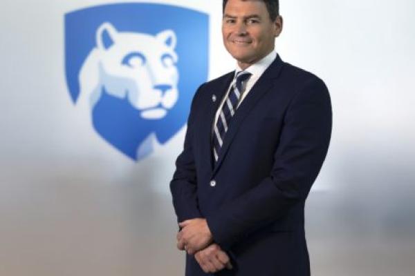 Dr. Michael Kupferman poses for a photo wearing a suit and tie. The Penn State Nittany Lion shield is in the background slightly out of focus.