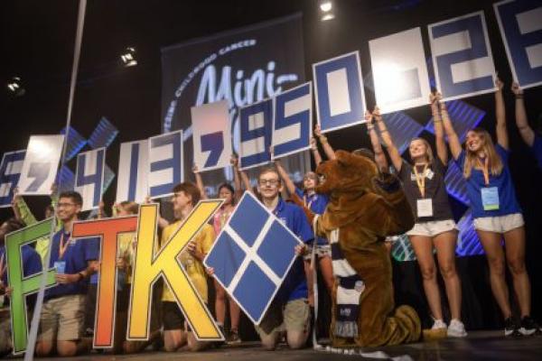 Several high school students, joined by the Nittany Lion, stand on stage and hold numbers - and the Four Diamonds logo - into the air.