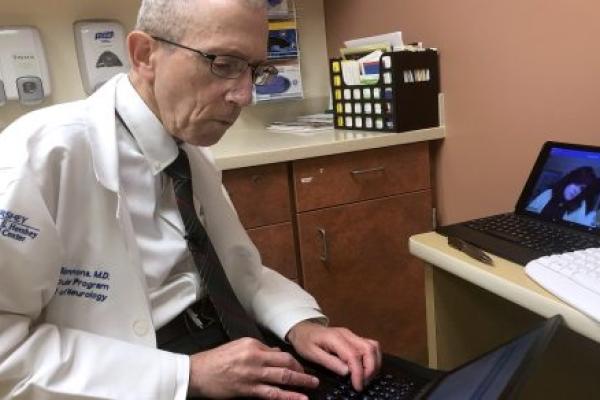 A doctor wearing a white coat types on a laptop.
