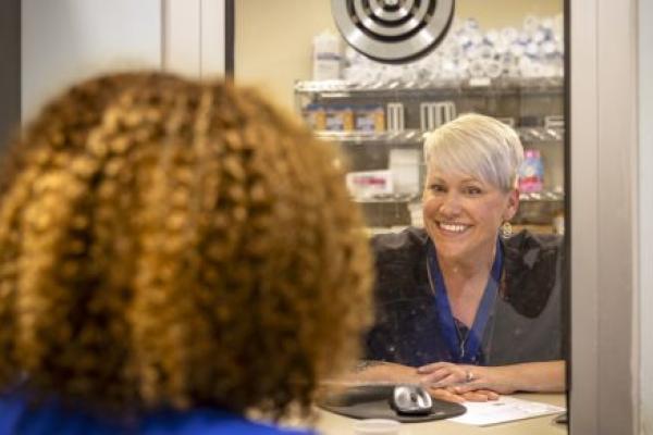 Lisa Duncan, an LPN with Penn State Health, smiles warmly to another woman through a dispensary window at the Pennsylvania Psychiatric Institute.