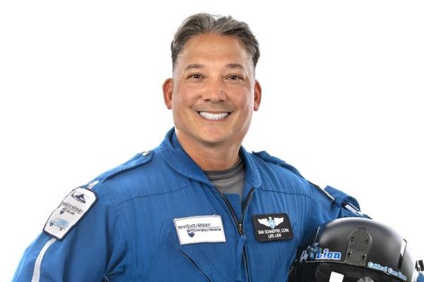 Daniel Schaeffer smiles at the camera in a blue uniform while holding a black helmet