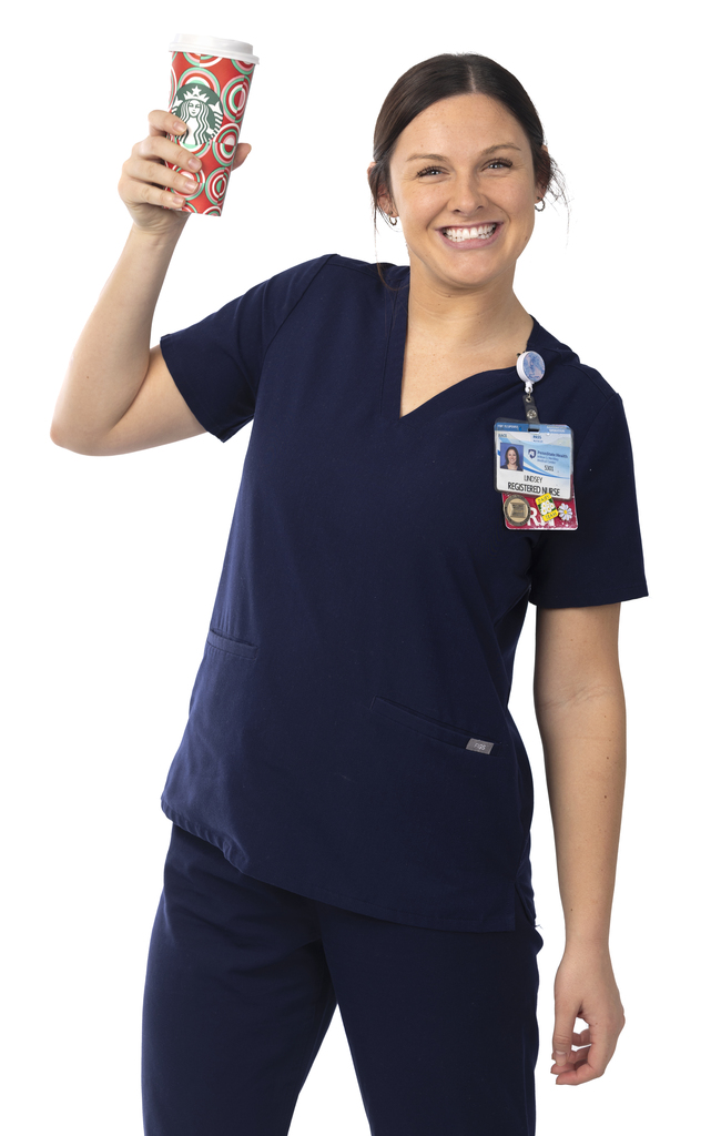 A female nurse is standing with a large cup from Starbucks and she is smiling.