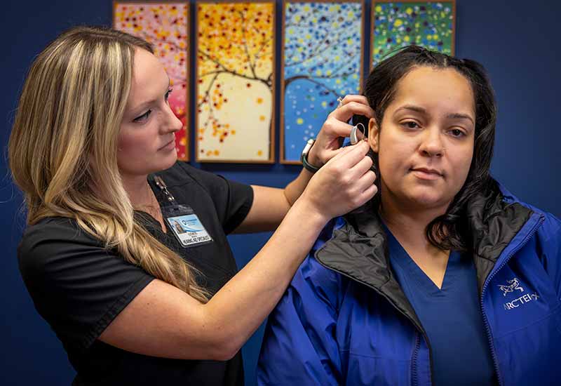 A hearing instrument specialist places a hearing aid in a patient's ear.